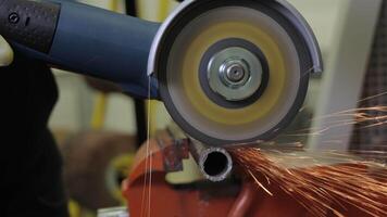 Worker using a high-speed angle grinder to cut a metal pipe with flying sparks, close-up view of a construction worker wearing gloves and operating grinding machine during work video