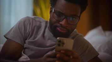 desapontado irritado africano americano homem masculino cara do utilizador cliente dentro Óculos conectados digitando mensagem mensagens de texto Móvel telefone conversando SMS aplicativo conflito cyberbullying problema erro às casa tarde quarto video