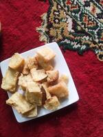 Photo of a plate of fried cassava. Fried food served on a white plate on a red Persian carpet. Traditional Indonesian cuisine. Soft and crunchy texture. Tasty Gourmet. Copy space and closeup