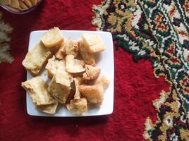 Photo of a plate of fried cassava. Fried food served on a white plate on a red Persian carpet. Traditional Indonesian cuisine. Soft and crunchy texture. Tasty Gourmet. Text space and closeup