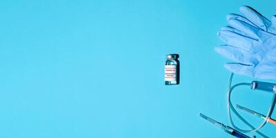 Vial of anti-covid vaccine, syringe with medicine and medical gloves on a blue background, flat lay. Banner with medical advice for vaccination, copy space. photo