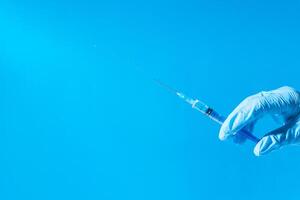 Hand in medical glove holding syringe with medicine, copy space. Injection with syringe on a blue background. Vaccination concept. photo
