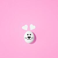 Creative minimal Easter concept. Rabbit face painted on egg with heart-shaped ears on pastel pink background. Flat lay. photo