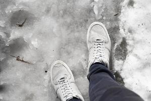 Legs in sneakers standing in the melting snow on the sidewalk. First-person view. Spring thaw concept photo