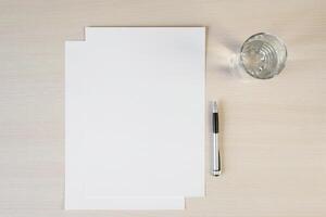Blank sheets of white paper, pen and glass of water on the table. Workplace, flat lay photo
