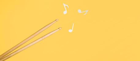 Drum sticks and music notes on a yellow background, copy space. Music banner, flat layout. photo
