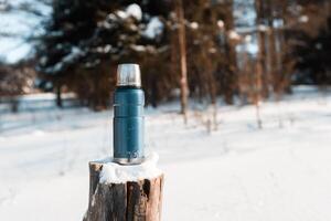 Thermos standing on a snowy stump in a winter forest on a sunny day. Trekking concept, camping photo