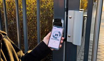 Young stylish woman getting access to the building by attaching smartphone to intercom. Concept of modern security technologies for access and smart home photo