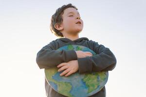 Little boy holding planet in hands against green spring background. Earth day photo