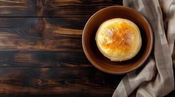 Golden baked bread roll in a bowl on wooden surface with linen cloth photo