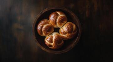 Fresh golden braided breads in a rustic wooden bowl on a dark surface photo