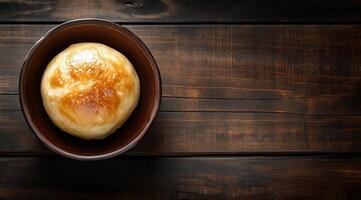 Golden baked bread roll on a rustic wooden table in dim light photo