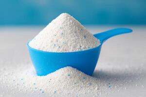 Scoop of White Powder in Blue Measuring Cup on Light Surface With Blue Background photo