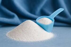 Washing Powder in Blue Scoop With Mound of Detergent on Soft Backdrop photo
