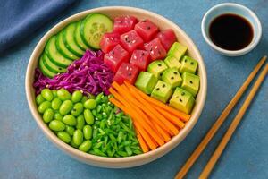 Colorful Fresh Vegetable and Fruit Bowl With Edamame and Dipping Sauce on a Blue Surface photo