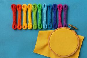 Colorful Embroidery Threads Arranged in a Rainbow Pattern Beside a Yellow Fabric and Embroidery Hoop photo