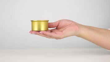 Hand offering golden container on neutral background. steady rotation sequence video