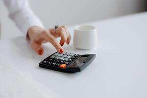 Calculating expenses with a calculator while enjoying a warm drink in a modern workspace photo