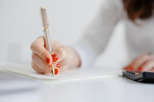 Woman writing notes with a pen and calculator on a desk during a work session in a bright, minimalist office space photo