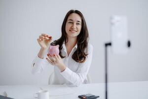 Woman saving money in piggy bank while connecting with others online during a virtual financial planning session photo