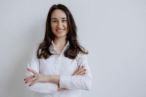 Young woman smiling confidently with arms crossed in front of a neutral background during a casual indoor setting photo