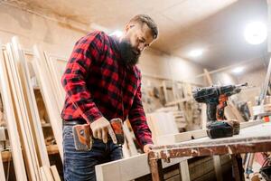 Skilled carpenter working in a workshop using a power drill to build wooden furniture photo