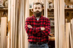 Craftsman stands confidently in woodworking shop surrounded by timber and tools in a cozy workshop environment photo