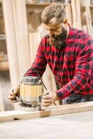 Skilled woodworker uses routing tool in workshop during daytime to shape wooden planks for custom furniture projects photo