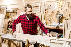 Woodworker shaping a plank in a workshop with tools and equipment during daytime photo