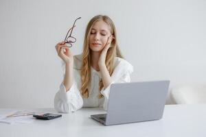 Confident young woman reflecting while working at a desk with a laptop on a bright day in a minimalist office photo