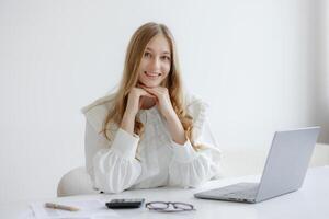 Young woman working at desk smiling with laptop during bright afternoon in minimalist workspace photo
