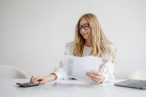 Young woman analyzes financial documents while using calculator in modern office setting during daylight hours photo