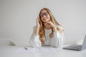 Young woman working at desk with laptop and documents while smiling in bright, modern office setting photo