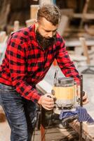 Craftsman working with a wood router in a workshop during daylight hours while wearing a plaid shirt photo