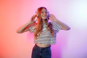 Young woman enjoying music with headphones while posing against a colorful background in a studio setting photo