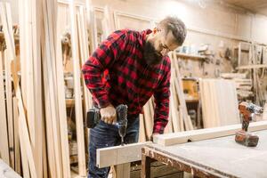 Craftsman using a power drill to work on wooden boards in a workshop during the day photo