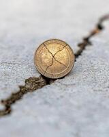 Cracked coin on concrete surface, symbolizing financial crisis or broken savings photo