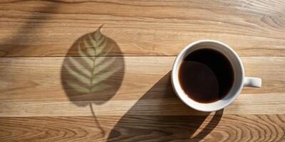 Coffee cup casting a leaf shadow on wooden table. photo