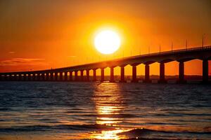 Sun setting behind a long bridge stretching over the water. photo