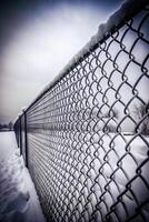 Close-up view of a snowy chain-link fence against a blurred background photo