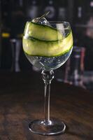 Assorted cocktails with orange, cucumber and berry garnishes served in balloon glasses on a rustic wood surface in a dimly lit bar, ideal for themes like bartending, drinks menu or nightlife photo