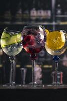Assorted cocktails with orange, cucumber and berry garnishes served in balloon glasses on a rustic wood surface in a dimly lit bar, ideal for themes like bartending, drinks menu or nightli photo