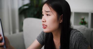 Handheld shot, Young Asian woman is having a heated argument with her boyfriend over a call while sitting on a sofa. Relationship problems video