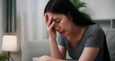 Handheld steady shot, Young Asian woman sit on the sofa alone, lost in thought. Her brows were slightly furrowed and expression tense in the quiet atmosphere at home video