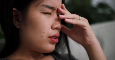 Handheld selective focus shot, Asian woman sit on the sofa alone, lost in thought. Her brows were slightly furrowed and expression tense in the quiet atmosphere at home video