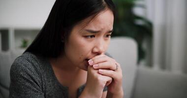 Handheld selective focus shot, Young Asian woman sit on the sofa alone, lost in thought. Her brows were slightly furrowed and expression tense in the quiet atmosphere. video