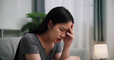 Handheld steady shot, Young Asian woman sit on the sofa alone, lost in thought. Her brows were slightly furrowed and expression tense in the quiet atmosphere at home. video