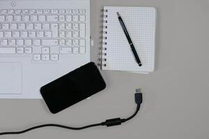 Flat lay on white background top view with copy space. Computer laptop keyboard, notebook, smartphone and cable. The concept of business, study or IT photo