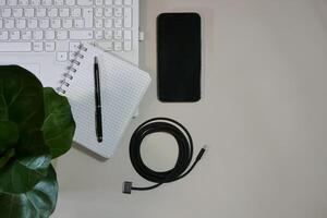 Flat lay on white background top view with copy space. Computer laptop keyboard, notebook, smartphone, house plant and cable. The concept of business, study or IT photo