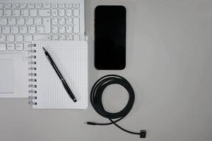 Flatlay on white background top view with copy space. Computer laptop keyboard, notebook, smartphone and cable. The concept of business, study or IT photo